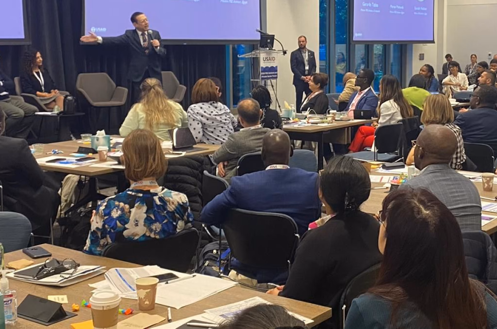 A speaker addressing a full room of executives seated at working tables